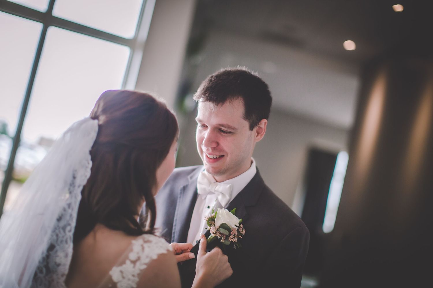 A tender wedding moment as a couple adjusts boutonniere in natural light.