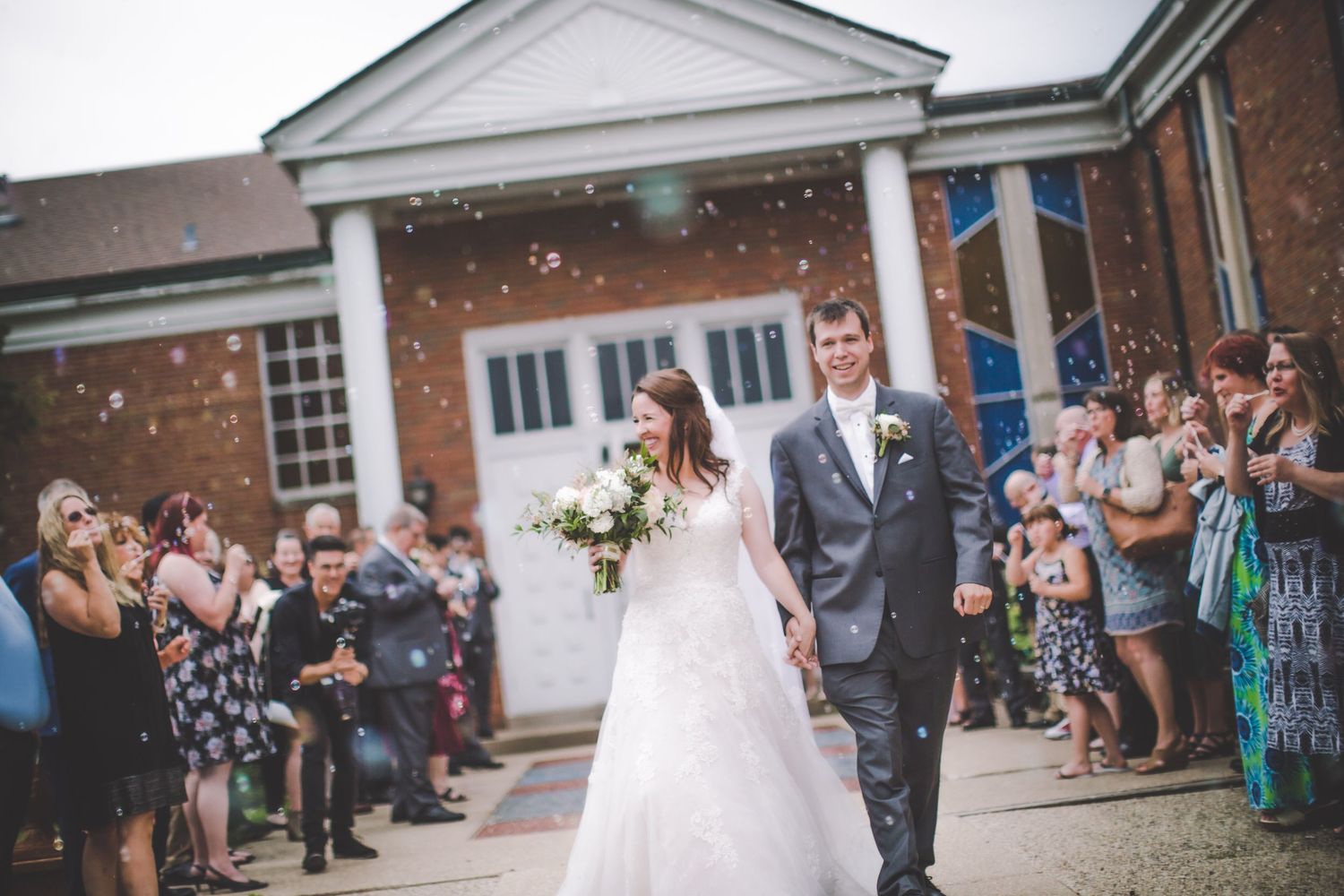 Wedding guests throwing confetti outside brick building with white columns.