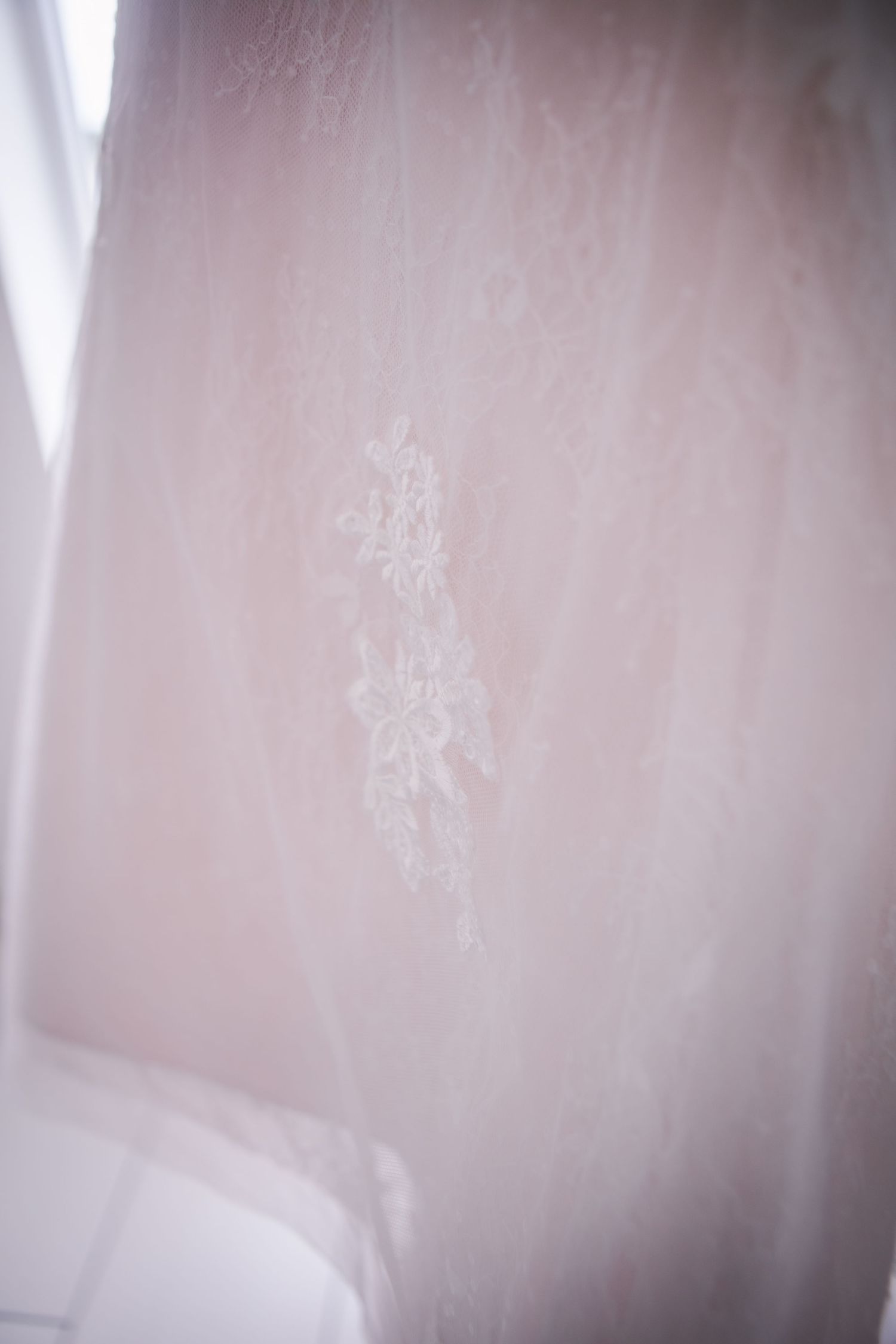Close-up details of delicate lace pattern on blush wedding gown fabric.