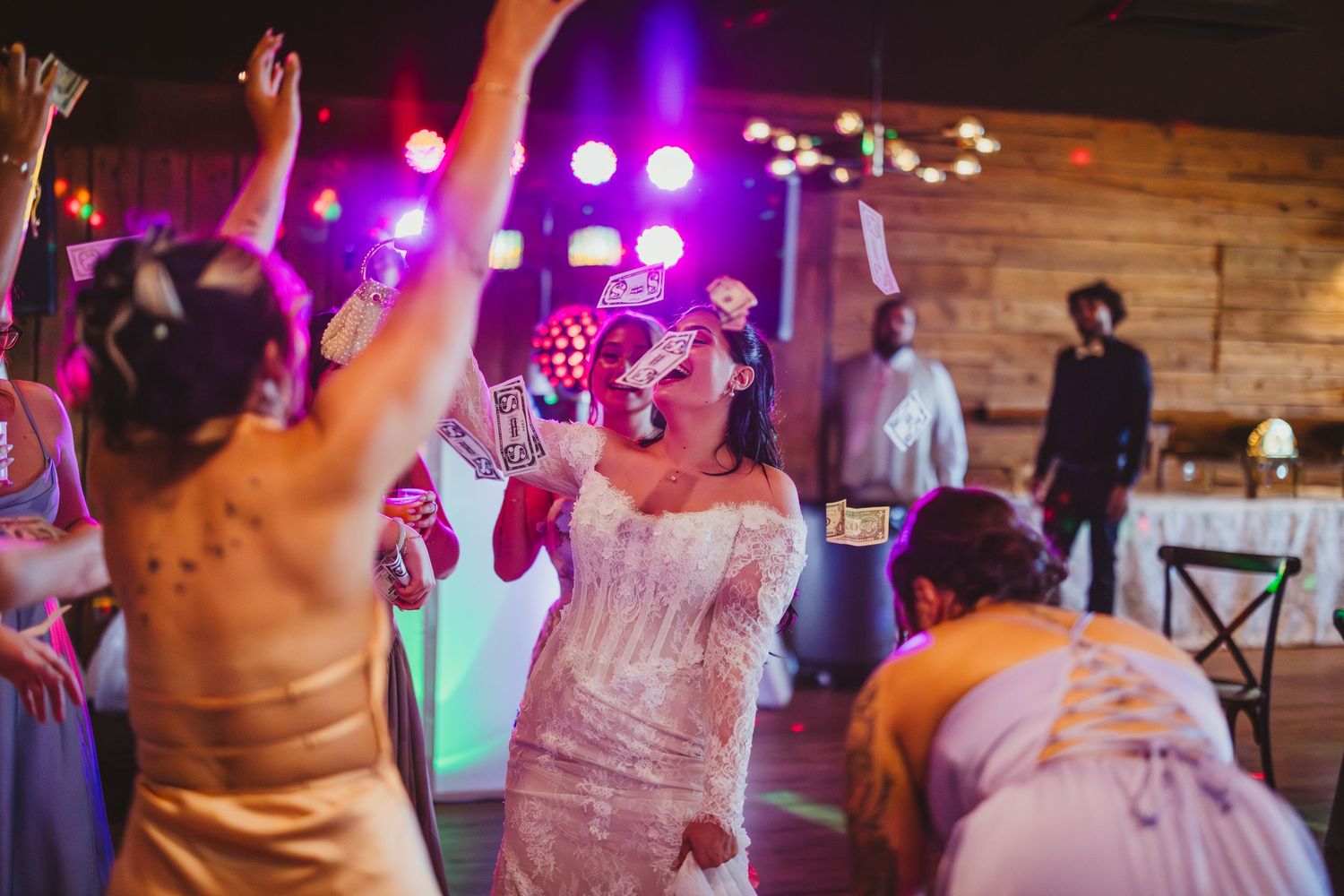 Bride singing into microphone on wedding dance floor with colorful stage lights and guests celebrating around her.