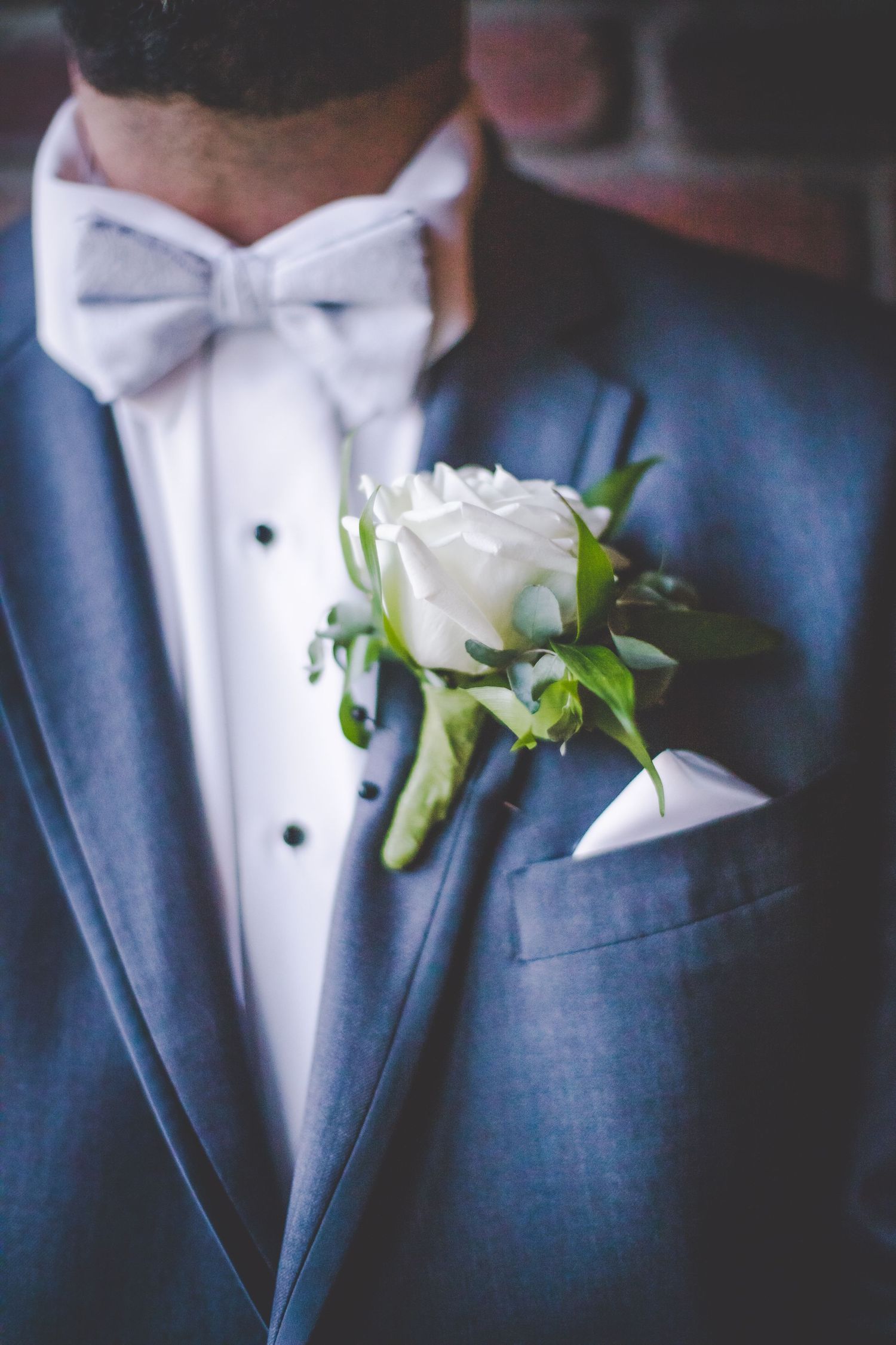 Elegant white rose boutonniere pinned to a navy blue tuxedo with white bow tie.