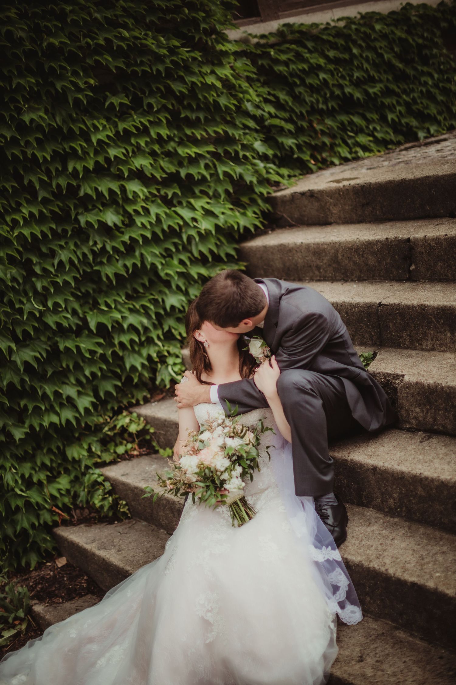 Intimate wedding portrait of couple sharing romantic moment on ivy-covered stone staircase.