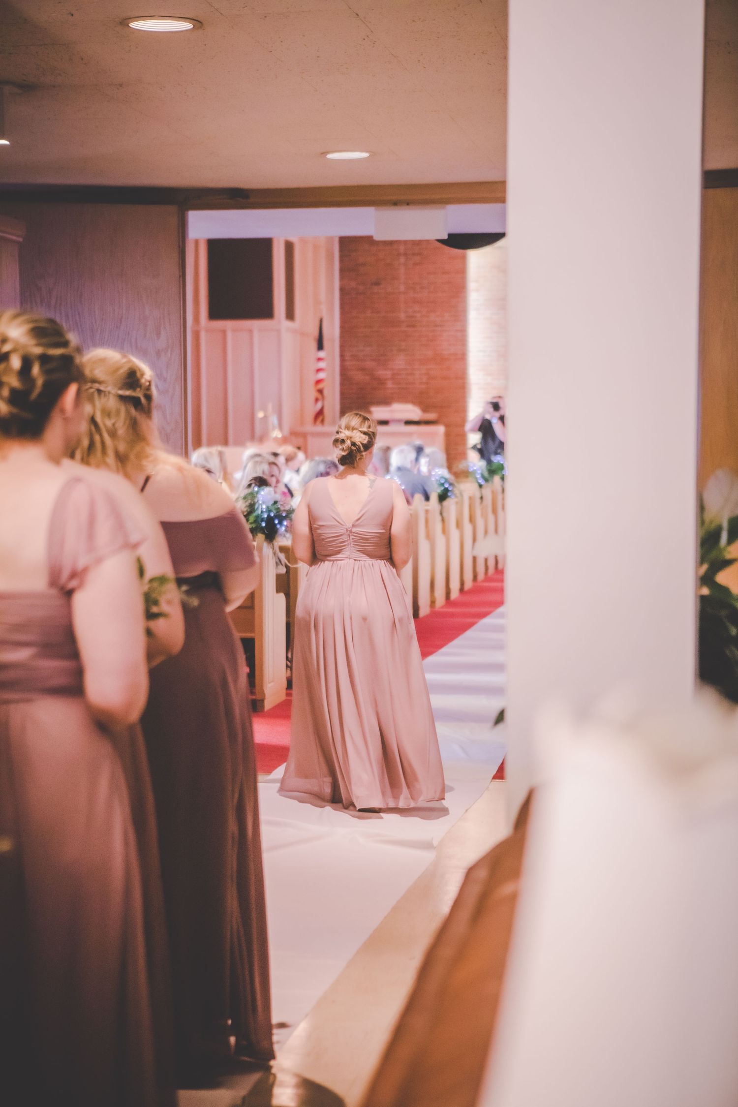 Pink-dressed bridesmaids stand in a church hallway during a wedding ceremony.