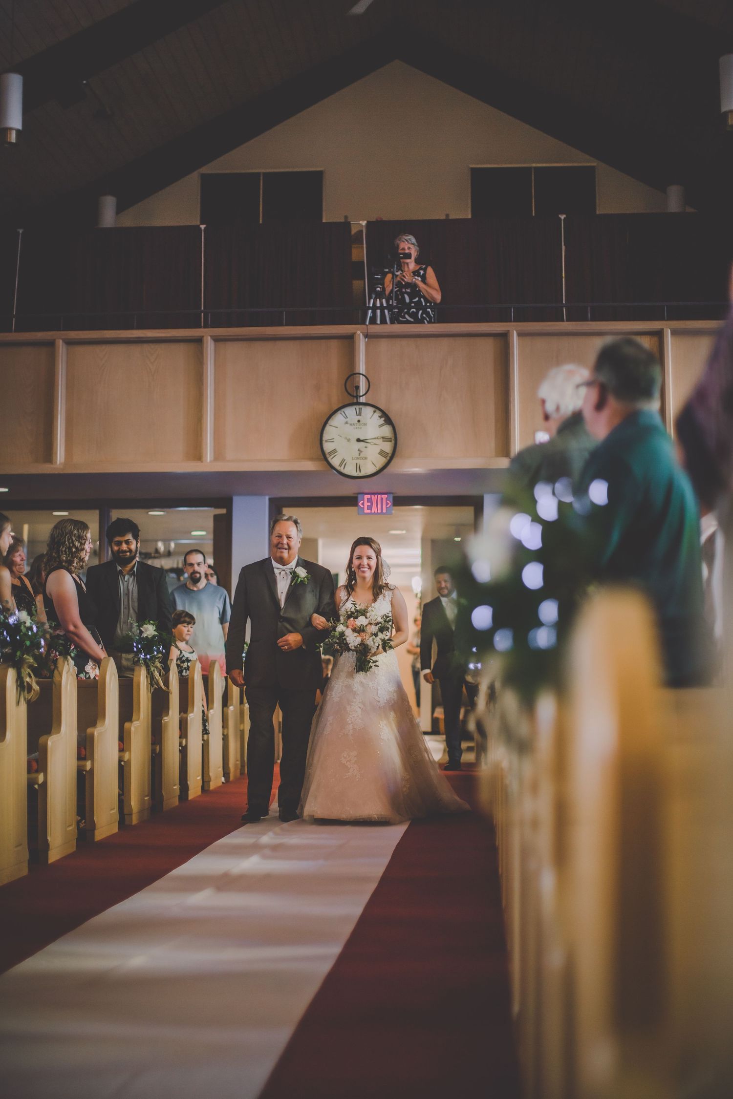 Wedding ceremony inside church sanctuary with long red carpeted aisle and wooden pews.