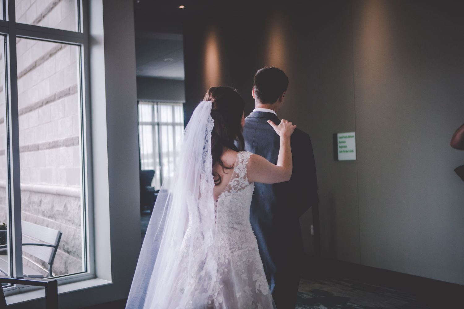 Intimate first look wedding moment captured from behind in natural window light.
