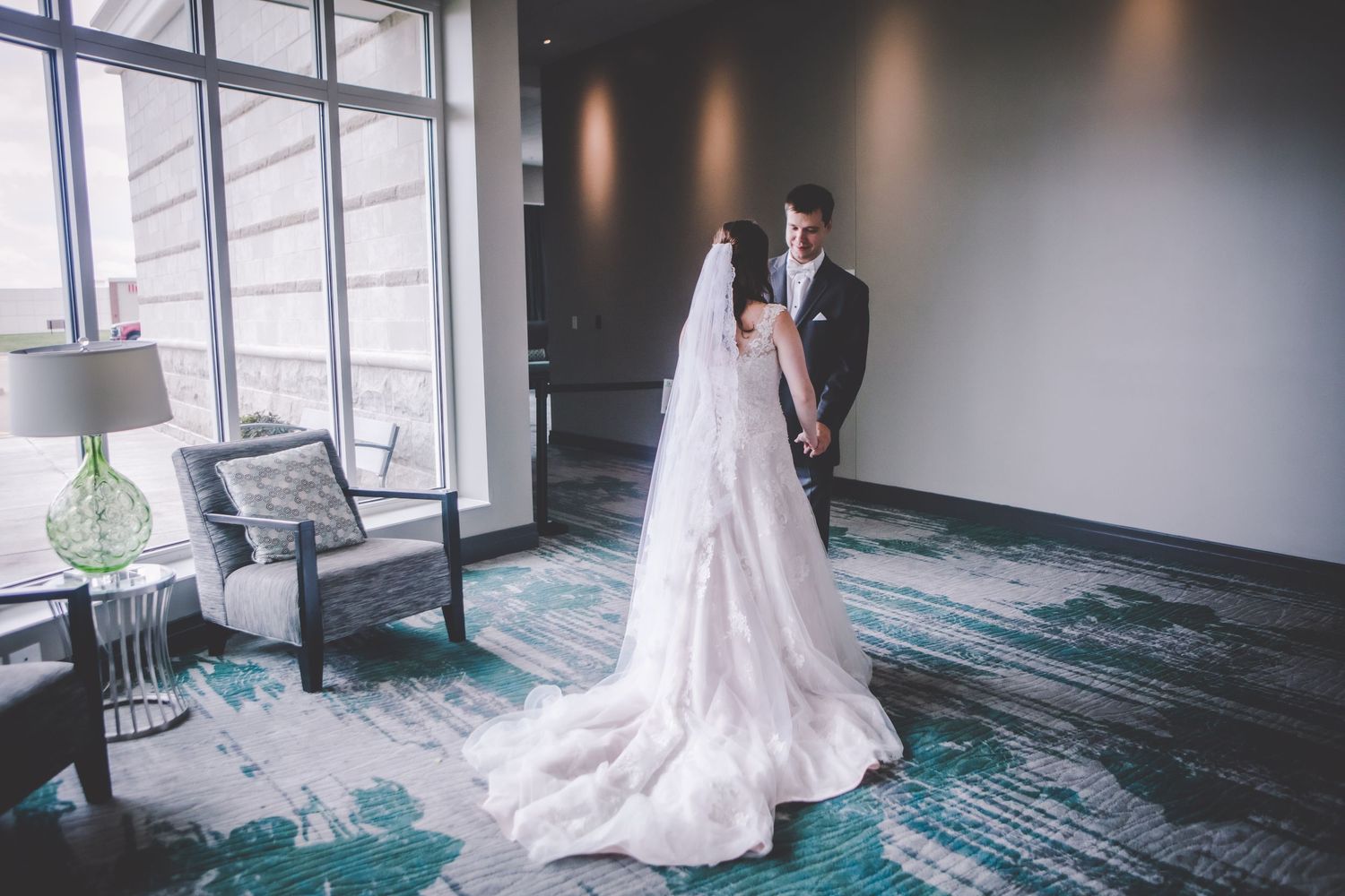 A bride and groom share an intimate moment in a modern hotel hallway with turquoise carpeting.