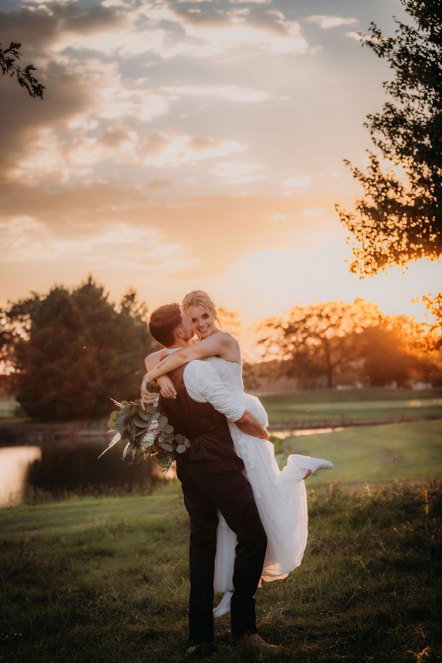 A romantic sunset wedding photo showing a couple's passionate embrace in a countryside setting.