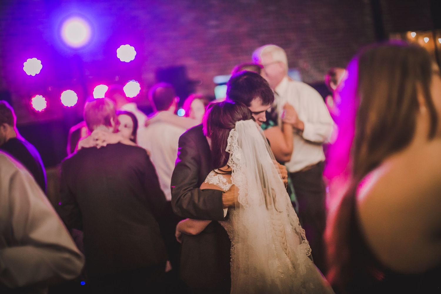 Purple and pink lighting illuminates a wedding reception dance floor.