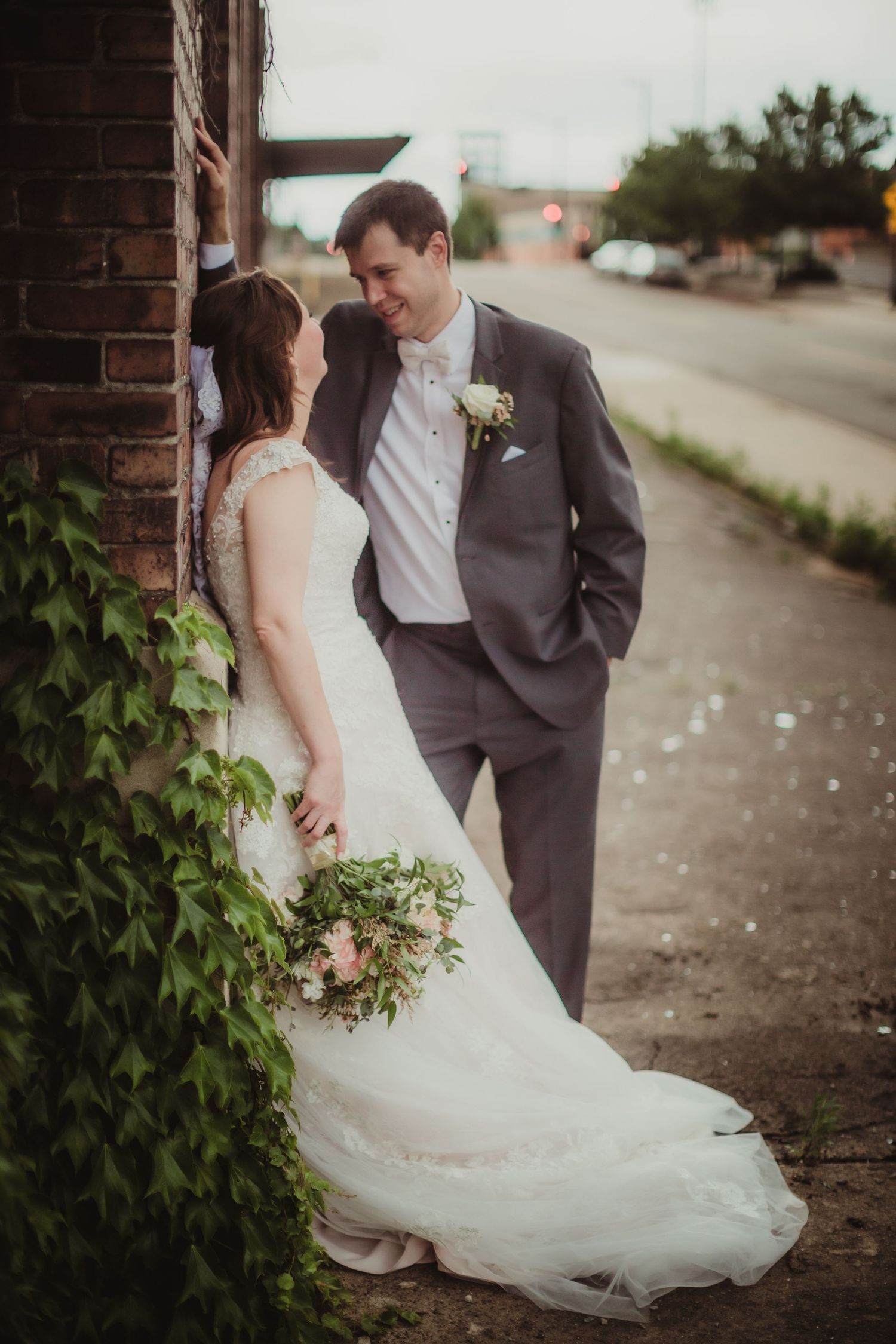 A romantic wedding portrait with ivy growing on brick wall as couple gazes at each other.