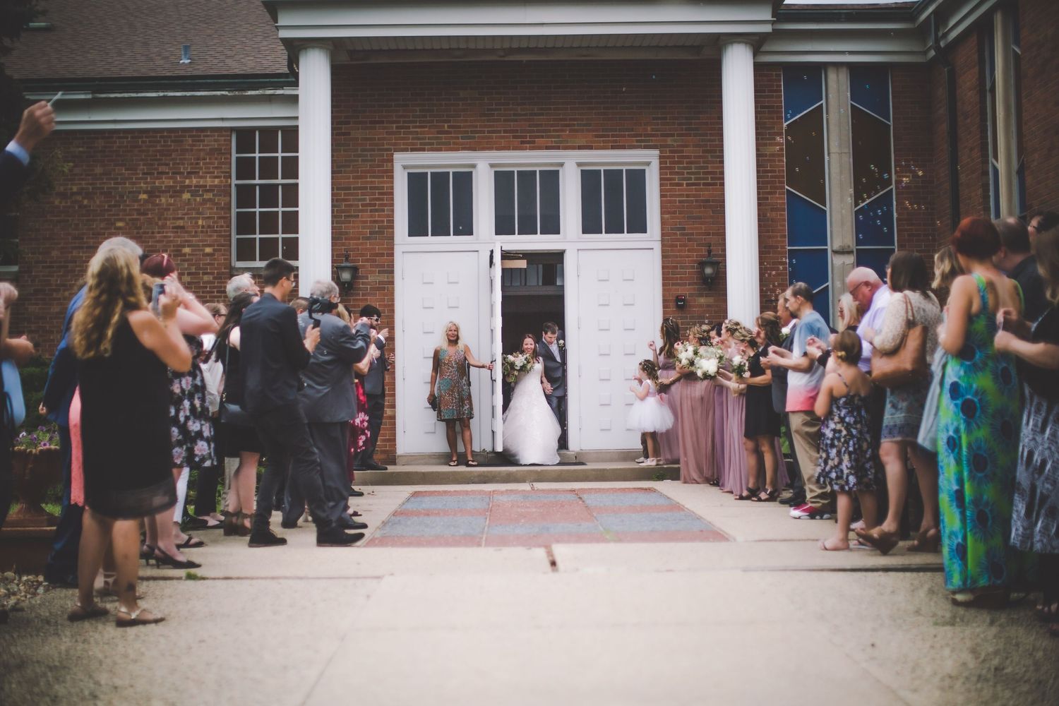Wedding guests line up outside brick church building entrance for reception departure.