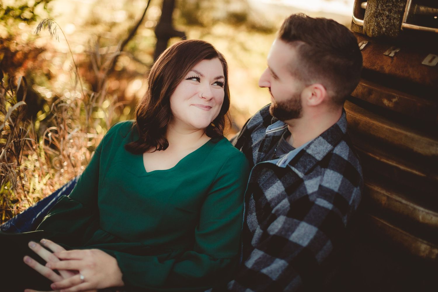 Romantic couple sharing tender moment against rustic cabin wall in autumn sunlight.