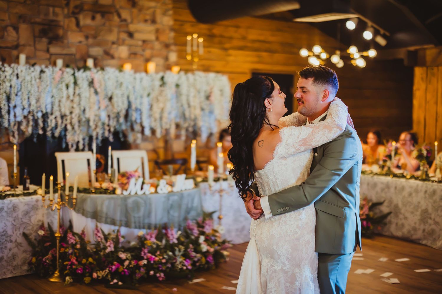Bride and groom share romantic first dance embrace in elegantly decorated rustic wedding venue.