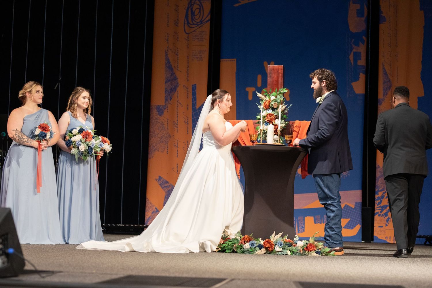 Couple performs unity ceremony at altar with bridesmaids in gray dresses watching.