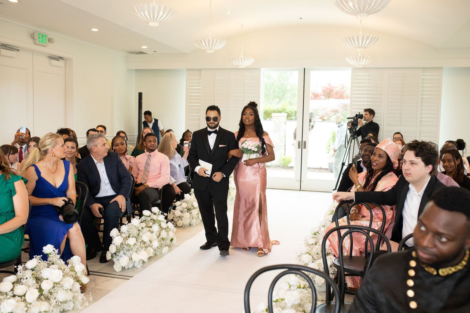Wedding ceremony room with modern decor, chandeliers, and seated guests in formal attire.