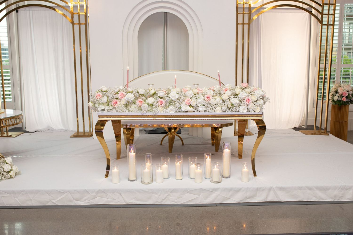 Elegant wedding sweetheart table with gold accents and floral arrangements on white platform.