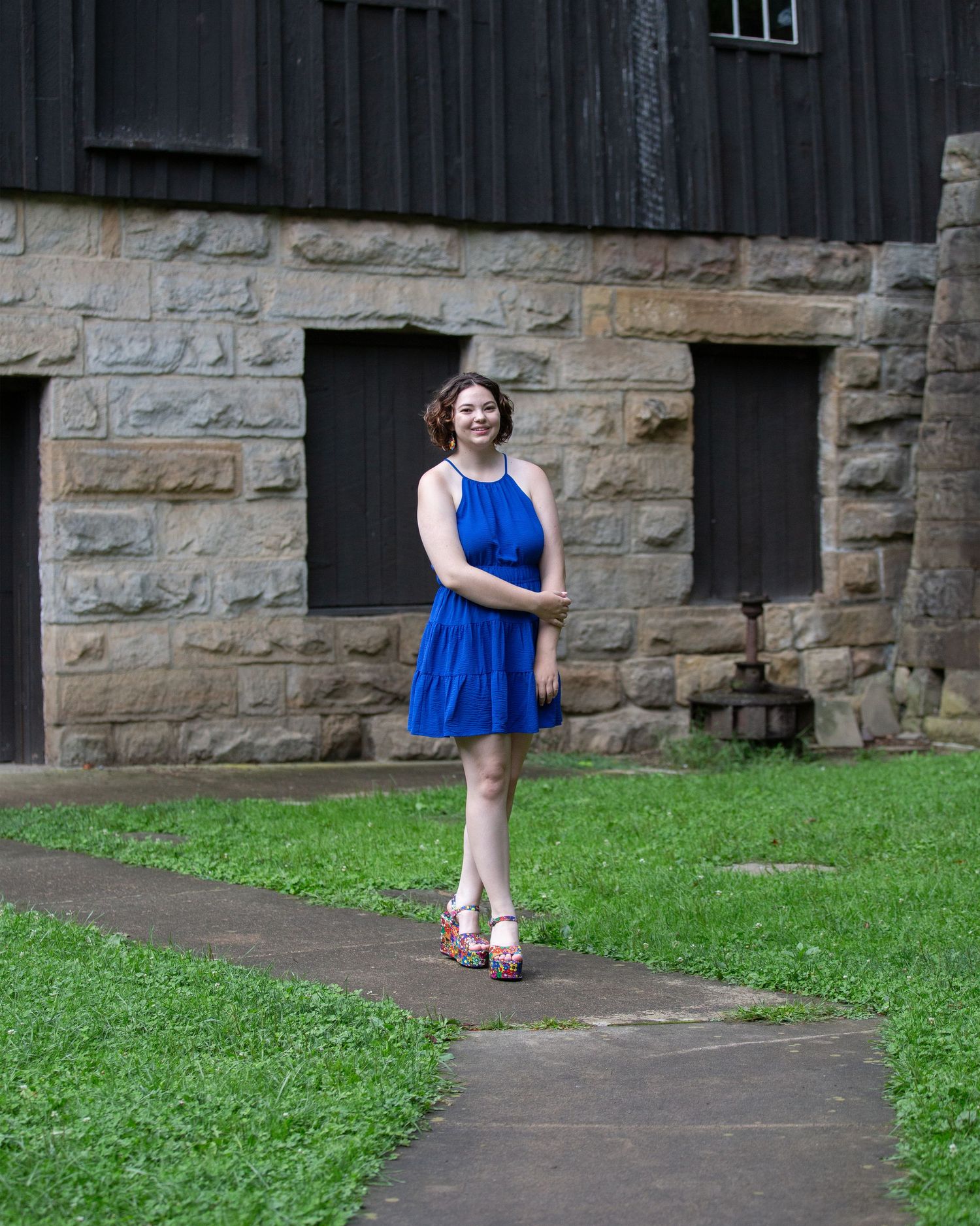Person in blue dress walking along stone building path with grass.