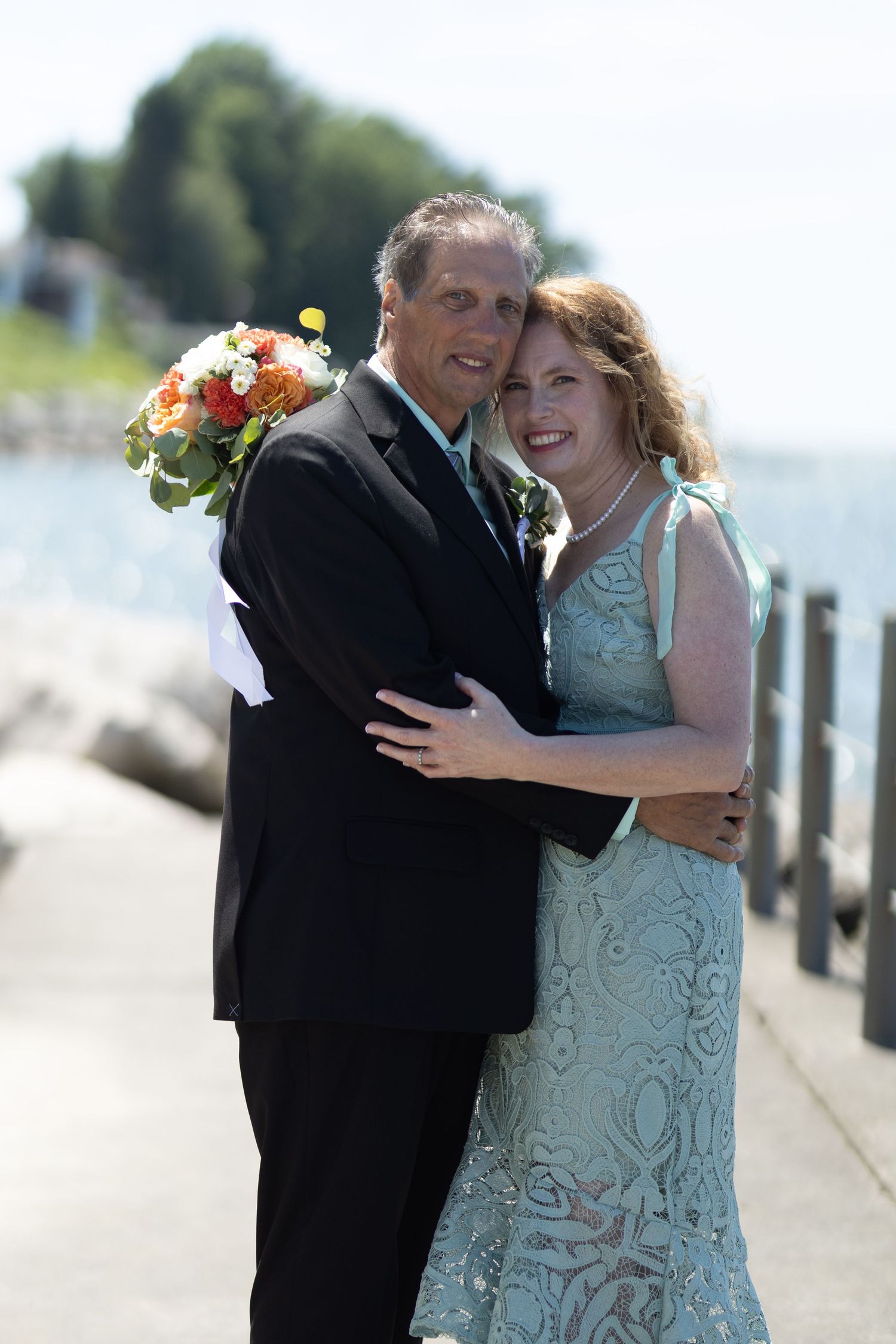 Couple embracing on a waterfront boardwalk after their wedding ceremony.