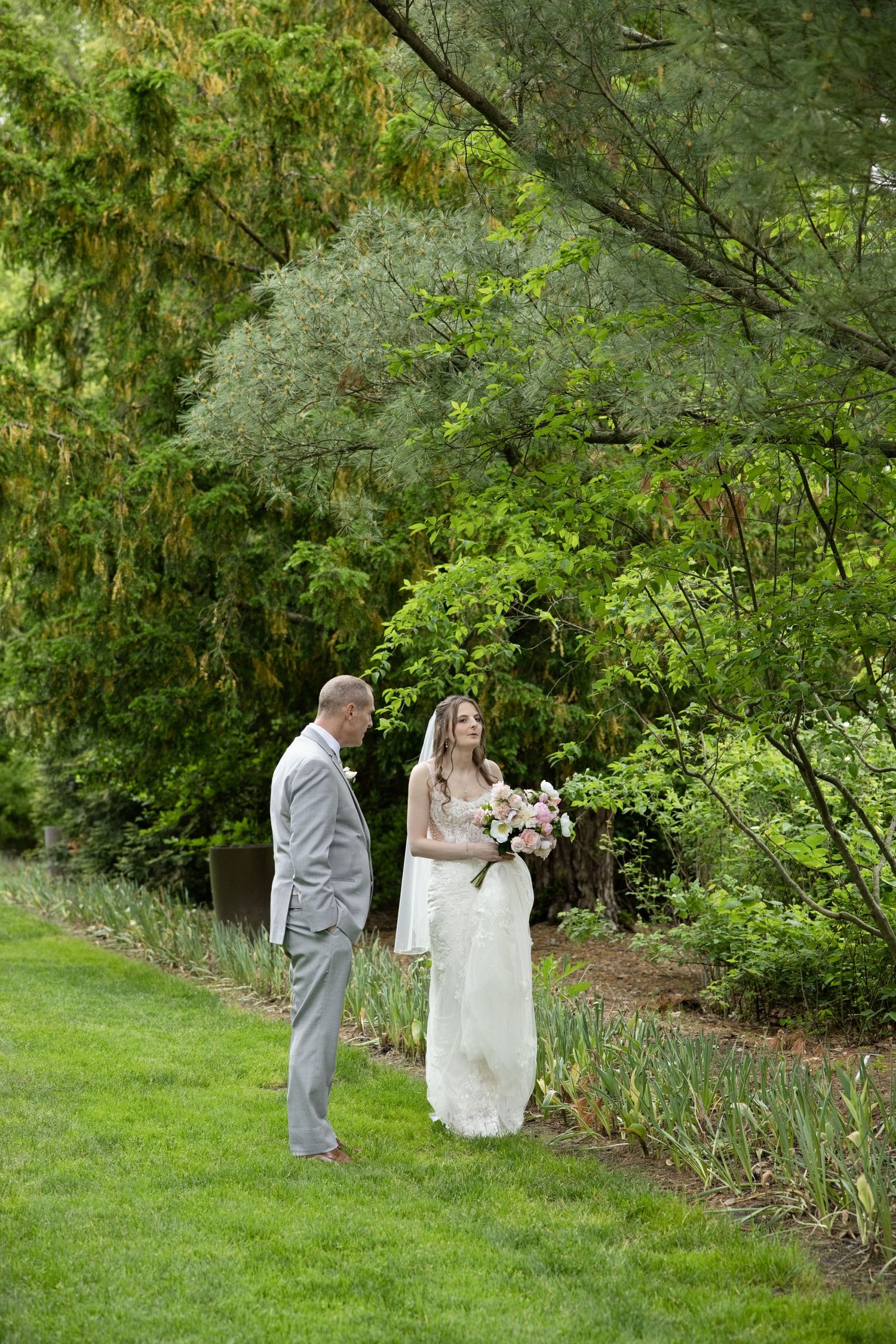 Bride and groom share a romantic first look moment in a lush green garden, bride holding a blush bouquet.