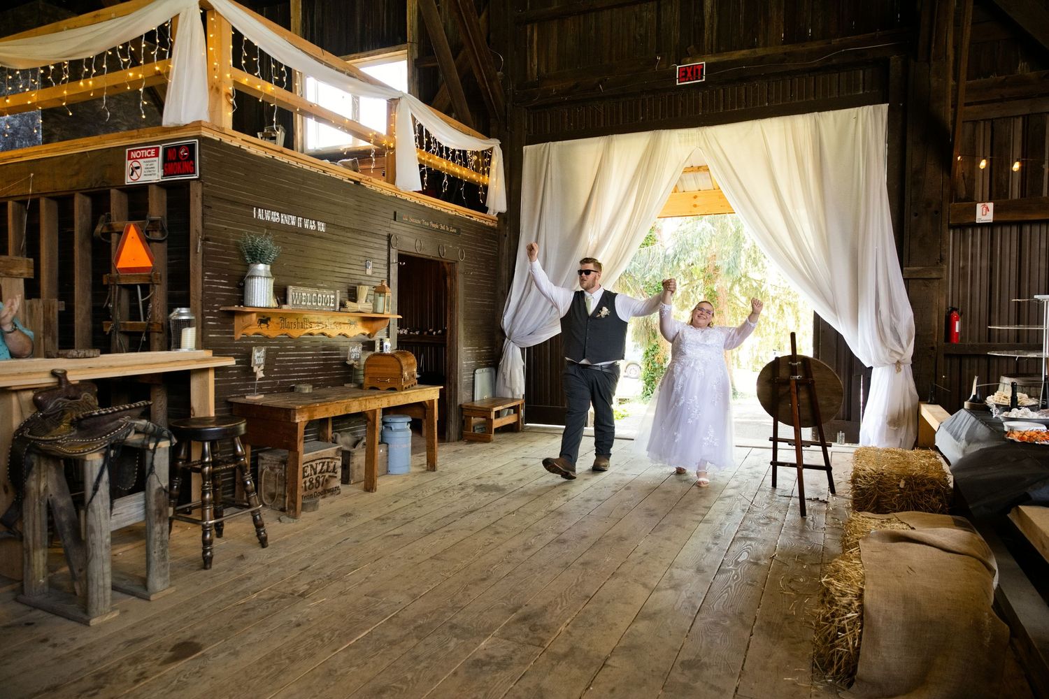 Bride and groom celebrate in a rustic barn wedding venue with white drape curtains and wooden decor.