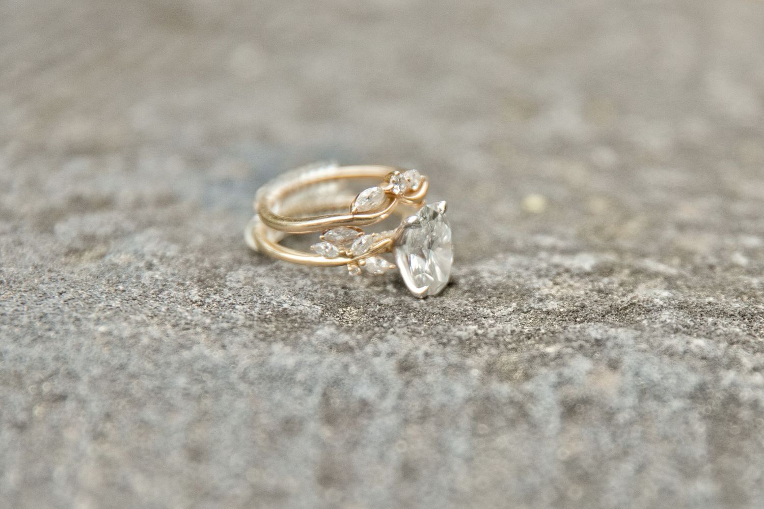 Gold ring set with pear-shaped white gemstone and delicate branch-style band, displayed on gray stone surface.