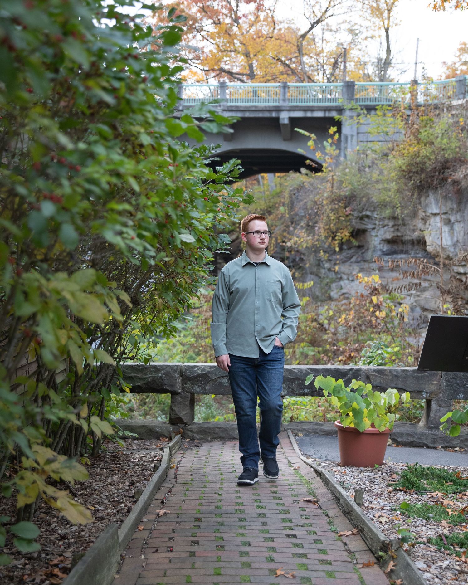 Person walks along brick pathway surrounded by autumn foliage and garden planters.