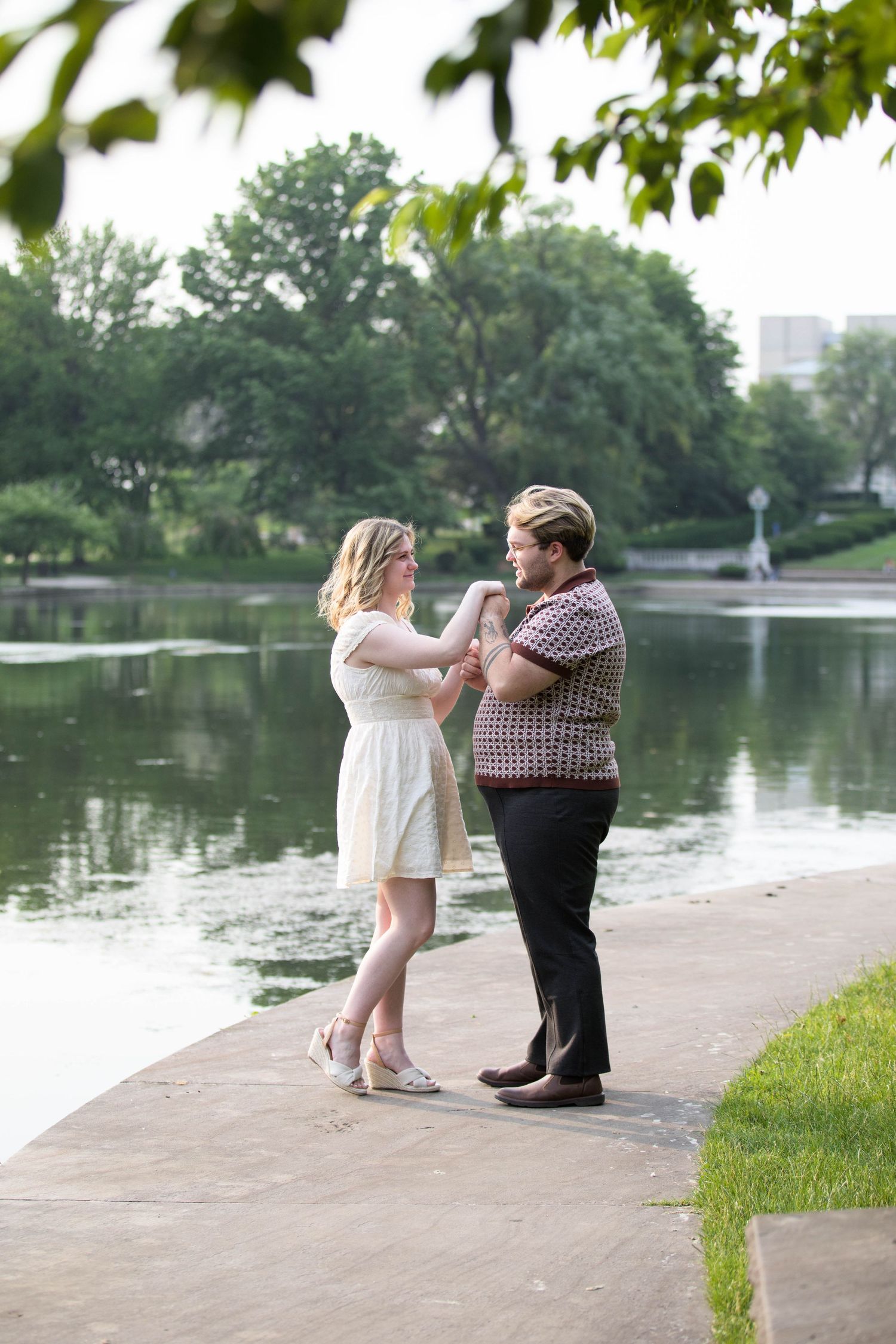 A couple shares an intimate moment by a pond in a scenic park setting.