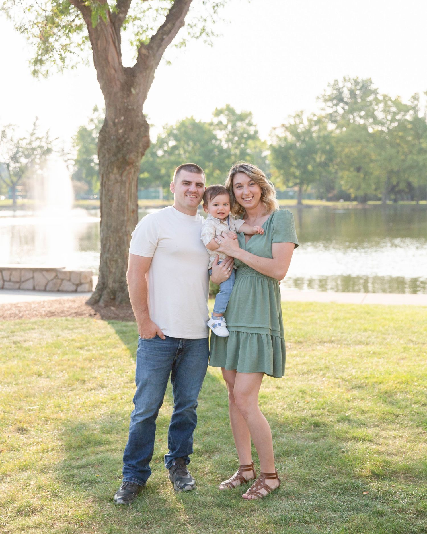 A family poses together under a tree with a fountain and lake in the background.