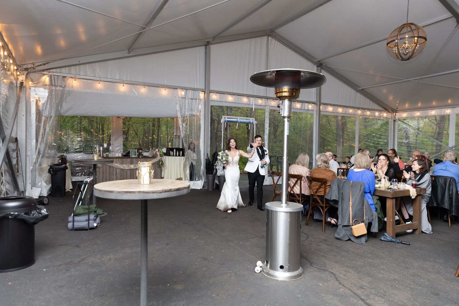 Elegant outdoor wedding reception under a white tent with string lights, patio heaters, and guests mingling near the dance floor.