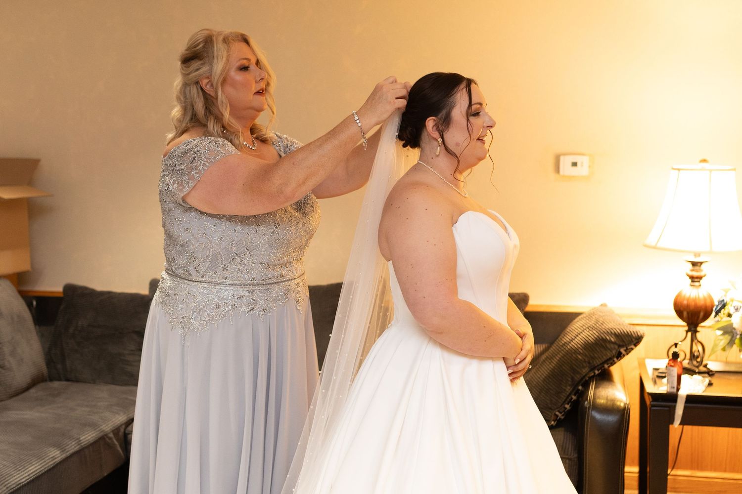 Final adjustments being made to a white wedding gown in a warmly lit room.