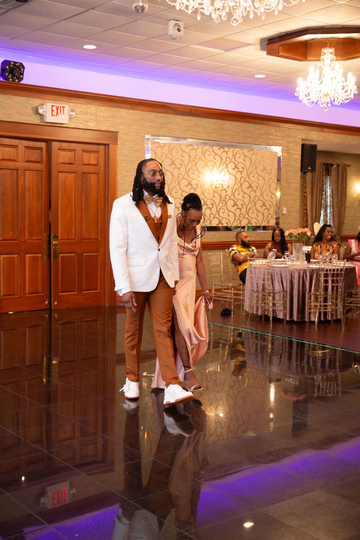Couples dancing at a wedding reception in a luxurious ballroom with wood paneling and chandeliers.