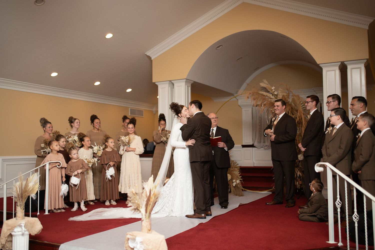 Formal wedding ceremony taking place in an elegant venue with arched doorways and red carpet.