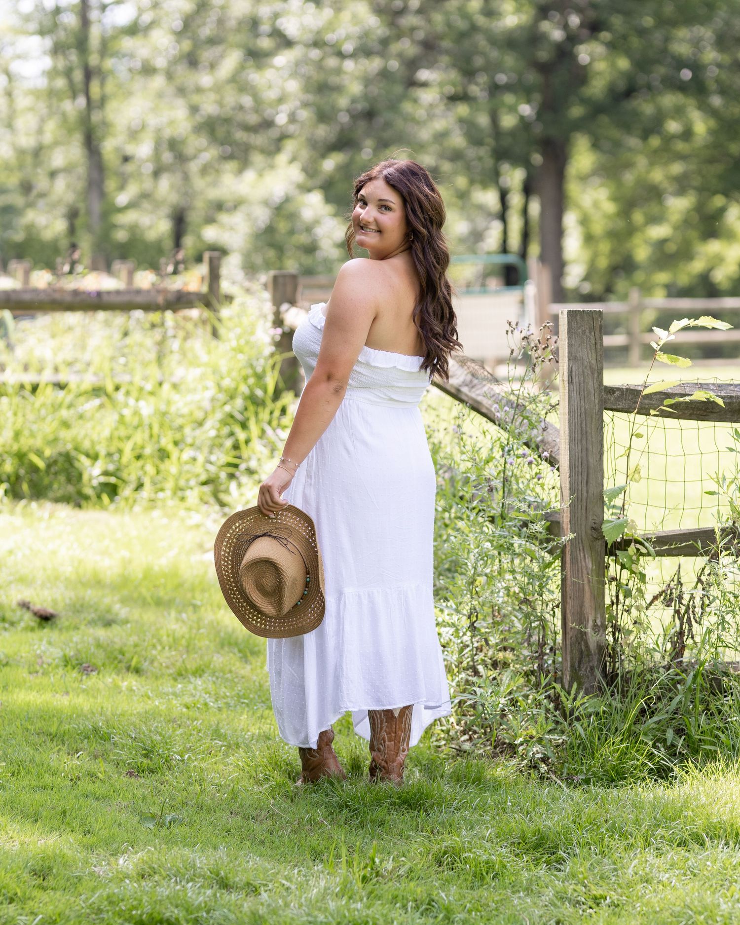 A white summer dress contrasts beautifully with the rustic wooden fence and green foliage.