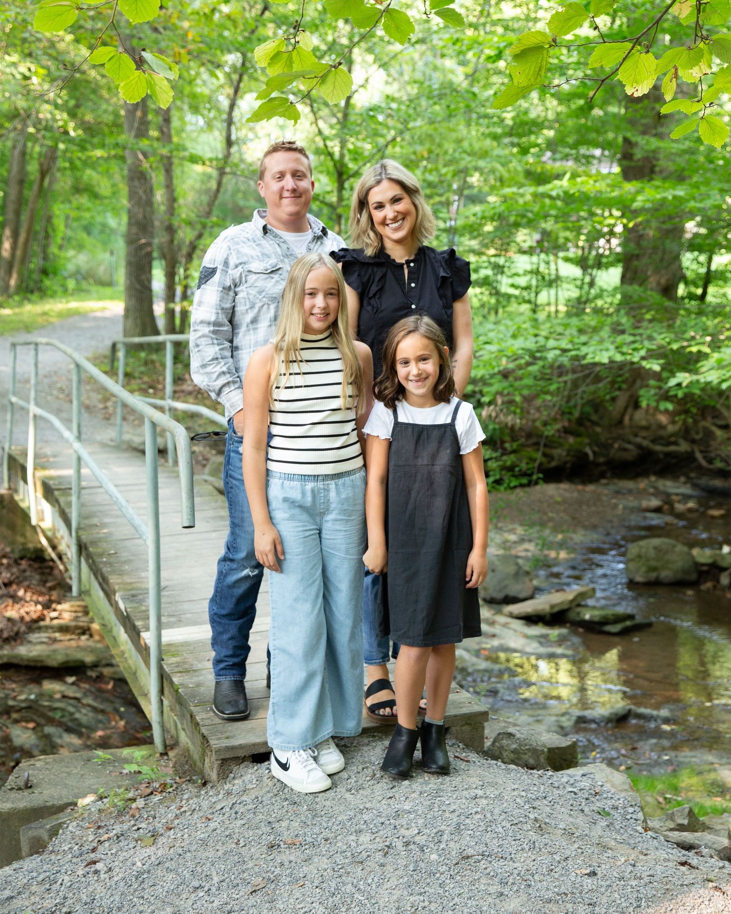 Group standing on gravel path near creek with rock formations and wooden railing.