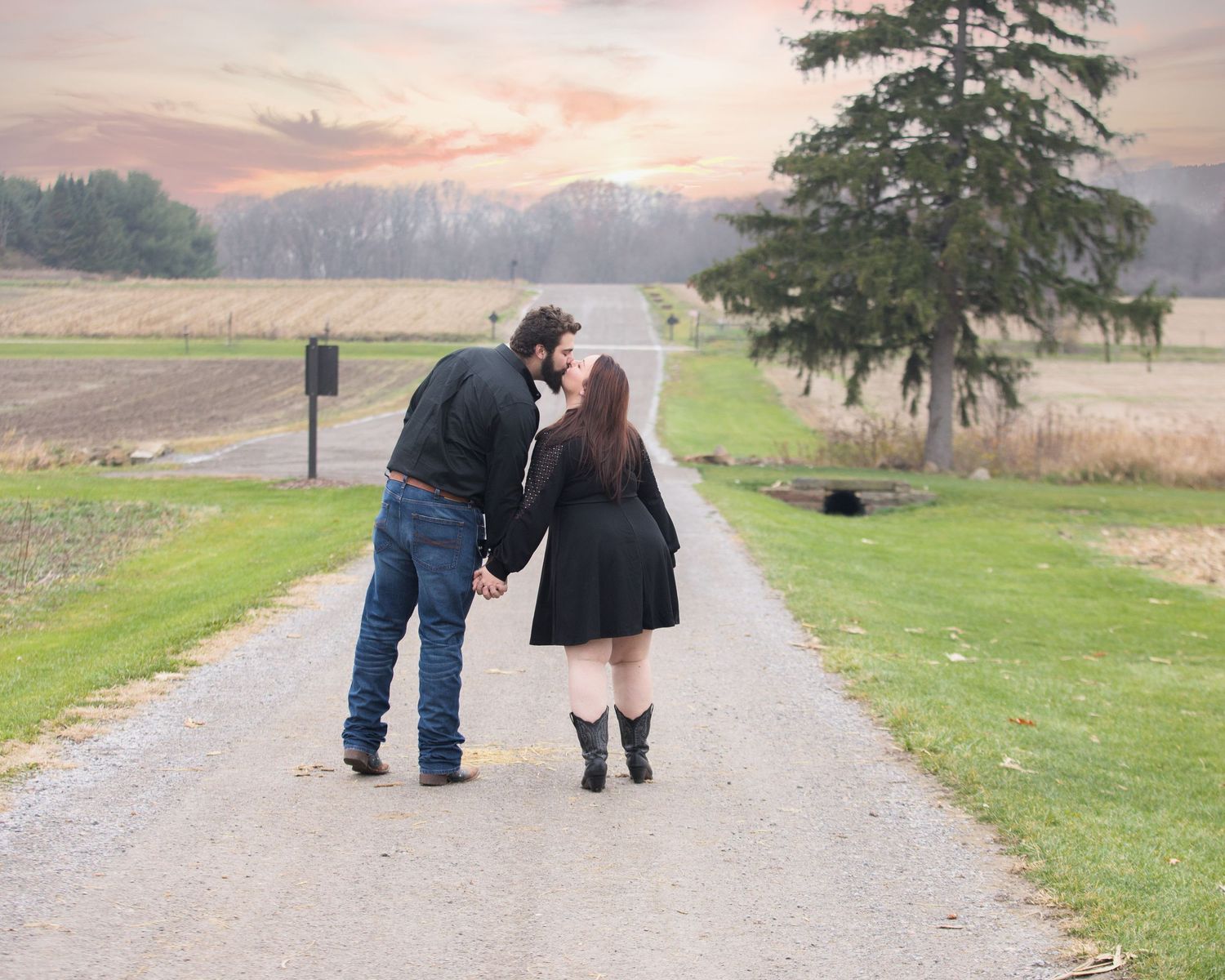 A couple shares an intimate moment on a rural path during sunset.