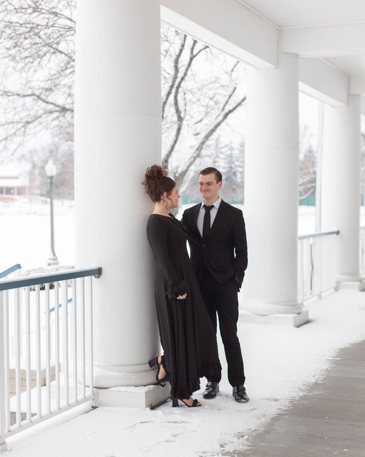 Couple in formal attire standing on snowy white porch with columns.