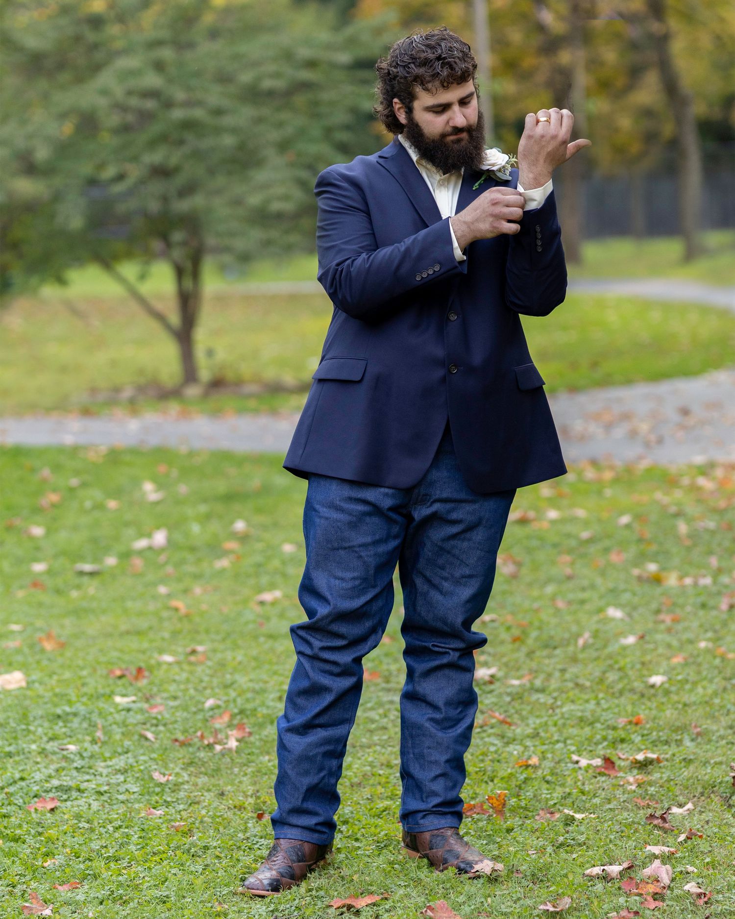 A groom in navy suit adjusts his boutonniere while standing outdoors.