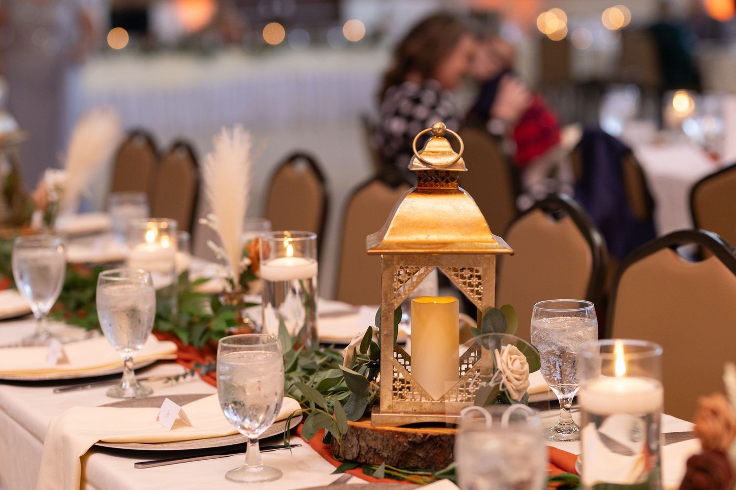 Wedding reception table decorated with gold lanterns, candles and greenery.