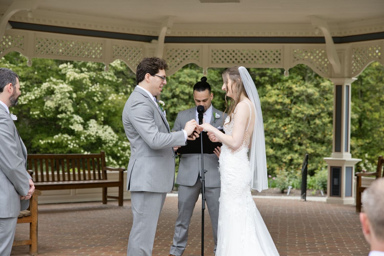 Bride and groom exchanging rings at outdoor gazebo wedding ceremony with officiant.