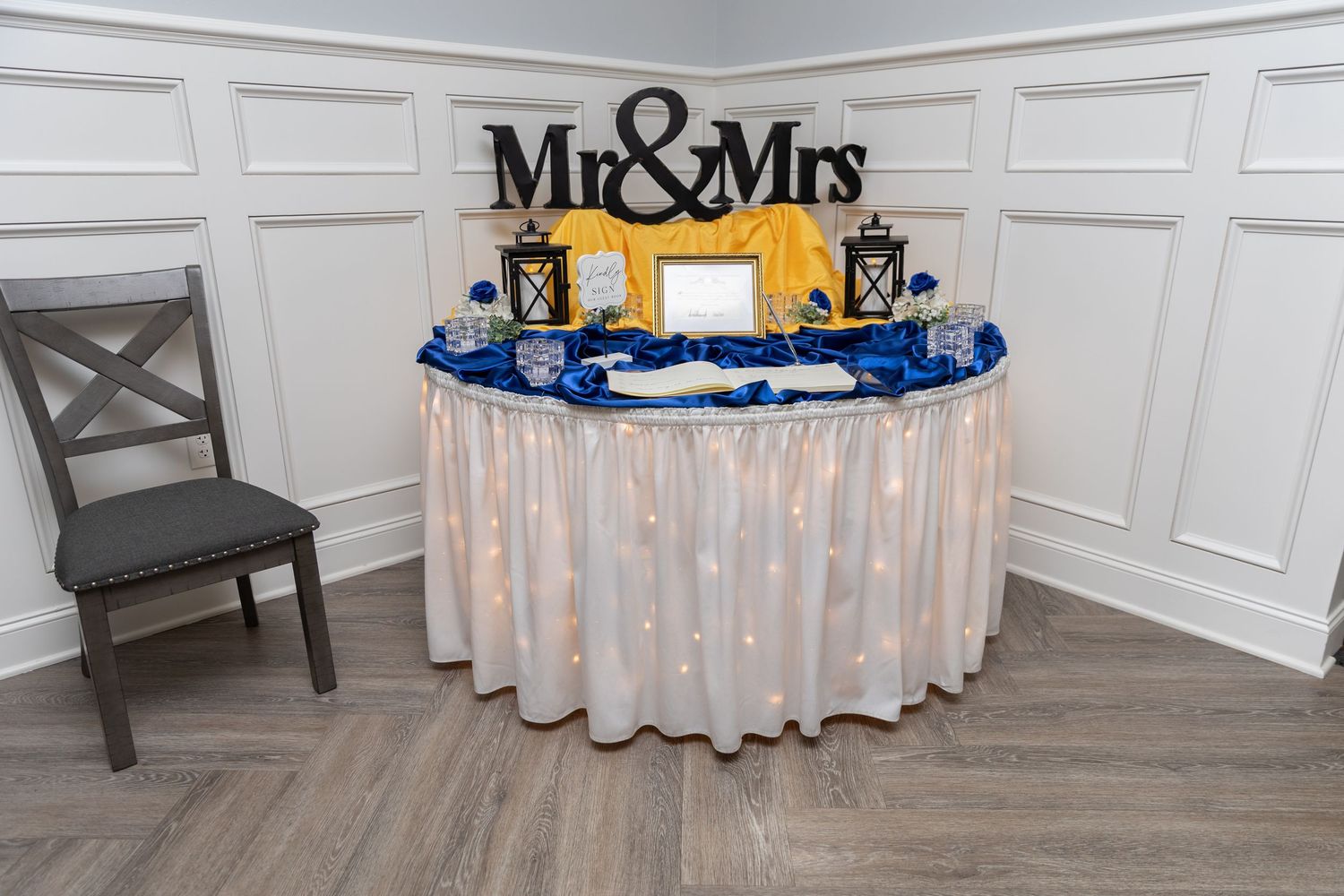 Elegant Mr. & Mrs. sweetheart table with royal blue and gold decor, fairy lights, and lanterns at a wedding reception.