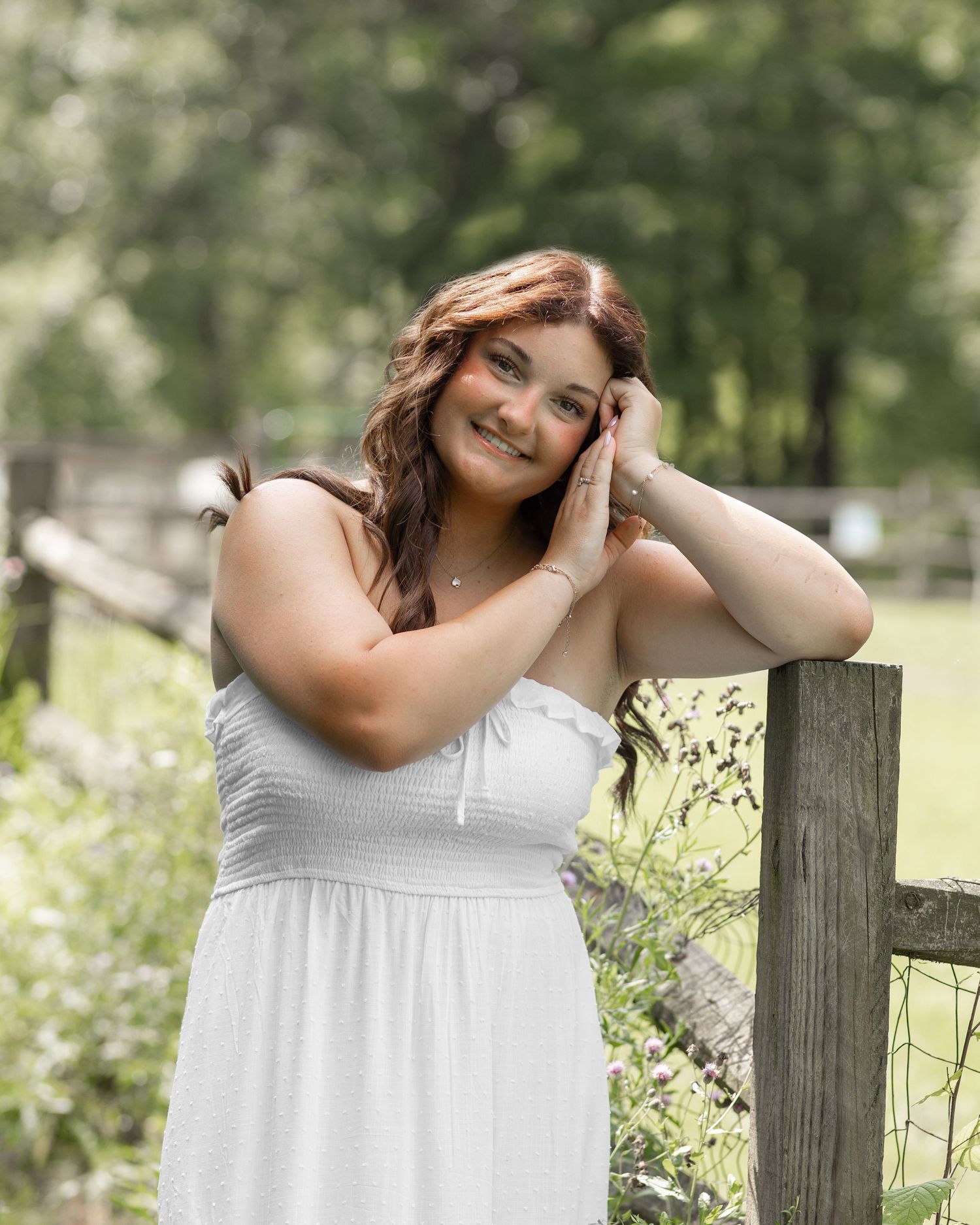 A serene outdoor portrait with someone leaning against a wooden fence in summer sunlight.