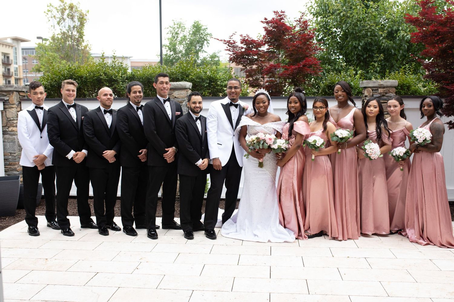 Large wedding party in pink and black attire posed together outdoors.