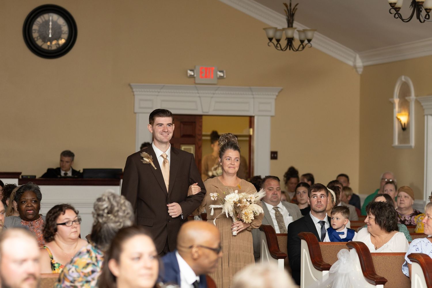 Wedding ceremony guests seated in rows watch attentively in an elegant venue with chandeliers and cream walls.