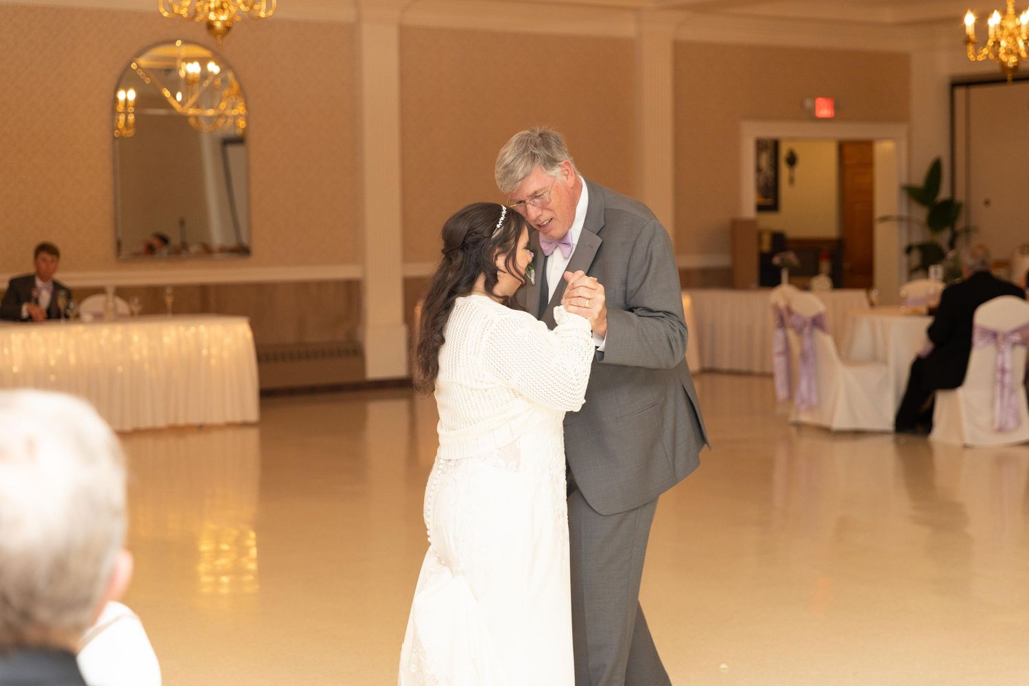 Bride and groom share their first dance on a white ballroom floor at an elegant wedding reception.