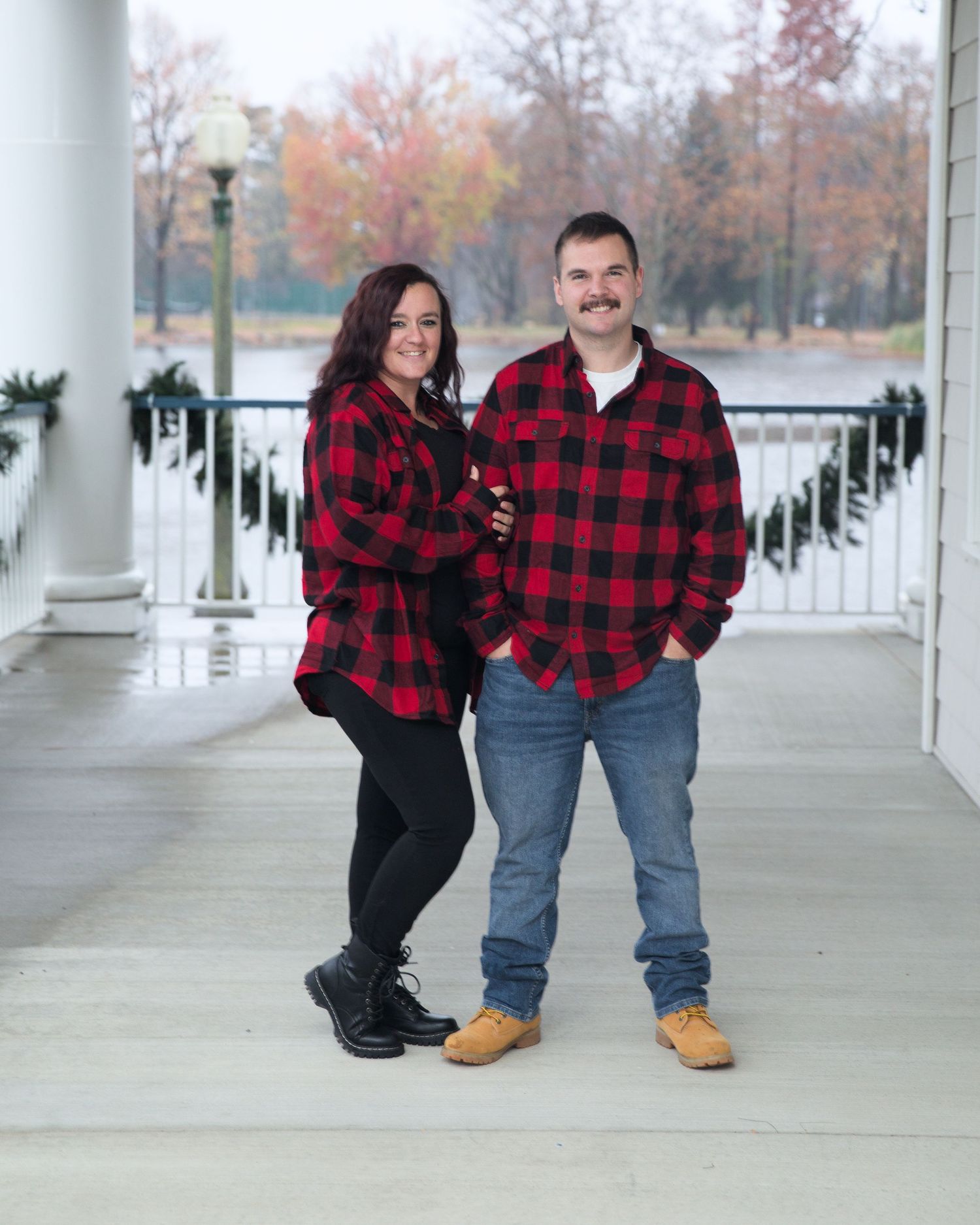 Family members in matching buffalo plaid shirts pose on a grand white porch.