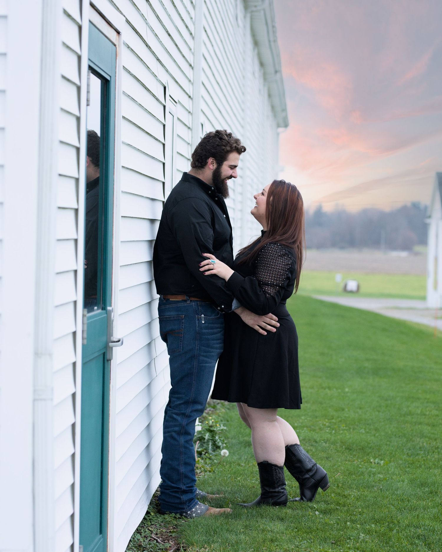 A romantic couple poses against a white building during sunset.