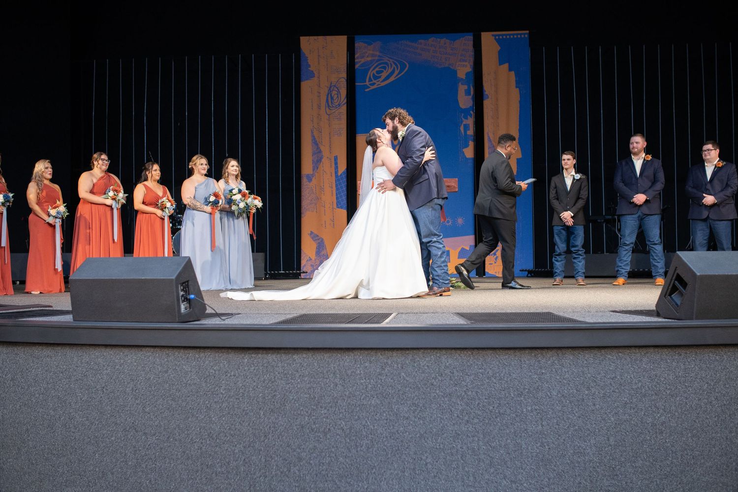 Wedding party lines up on stage with bridesmaids in coral and gray dresses during ceremony.