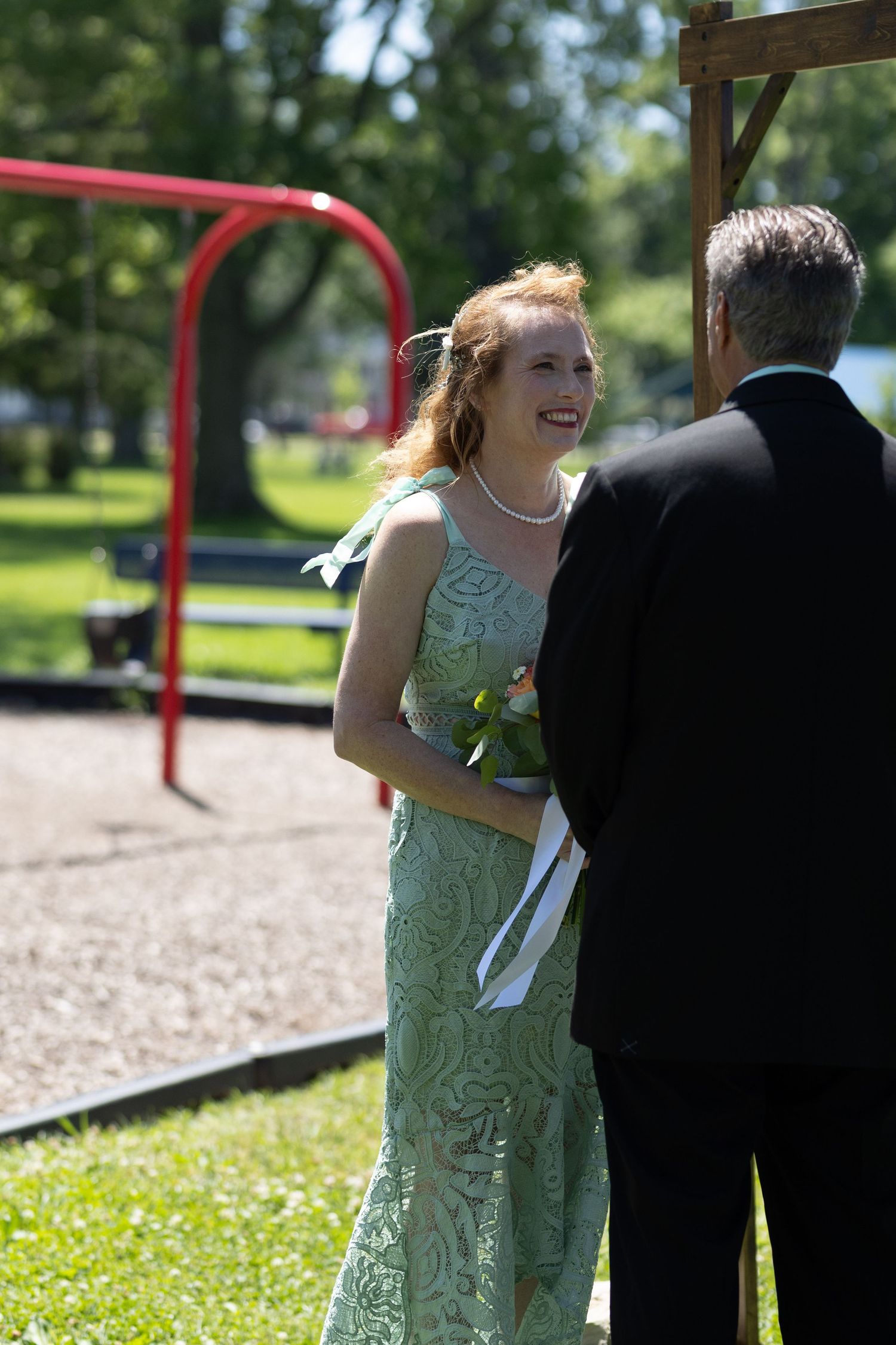 A couple exchanges vows during an intimate outdoor wedding ceremony under a wooden arch.