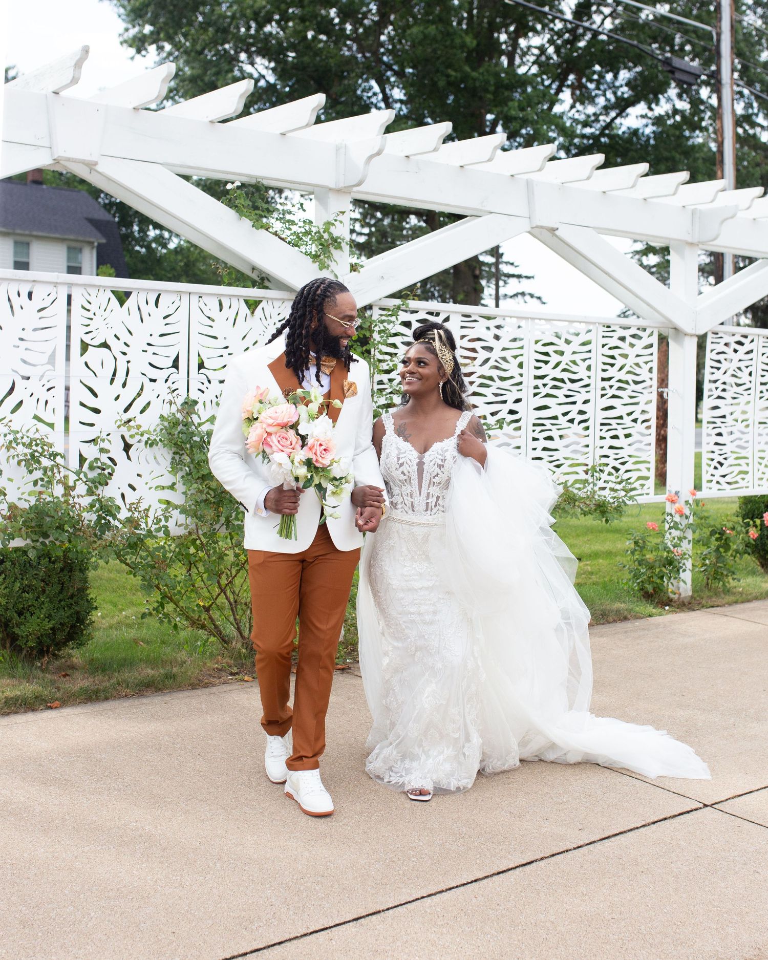 Newlyweds walking together under white pergola with decorative panels.