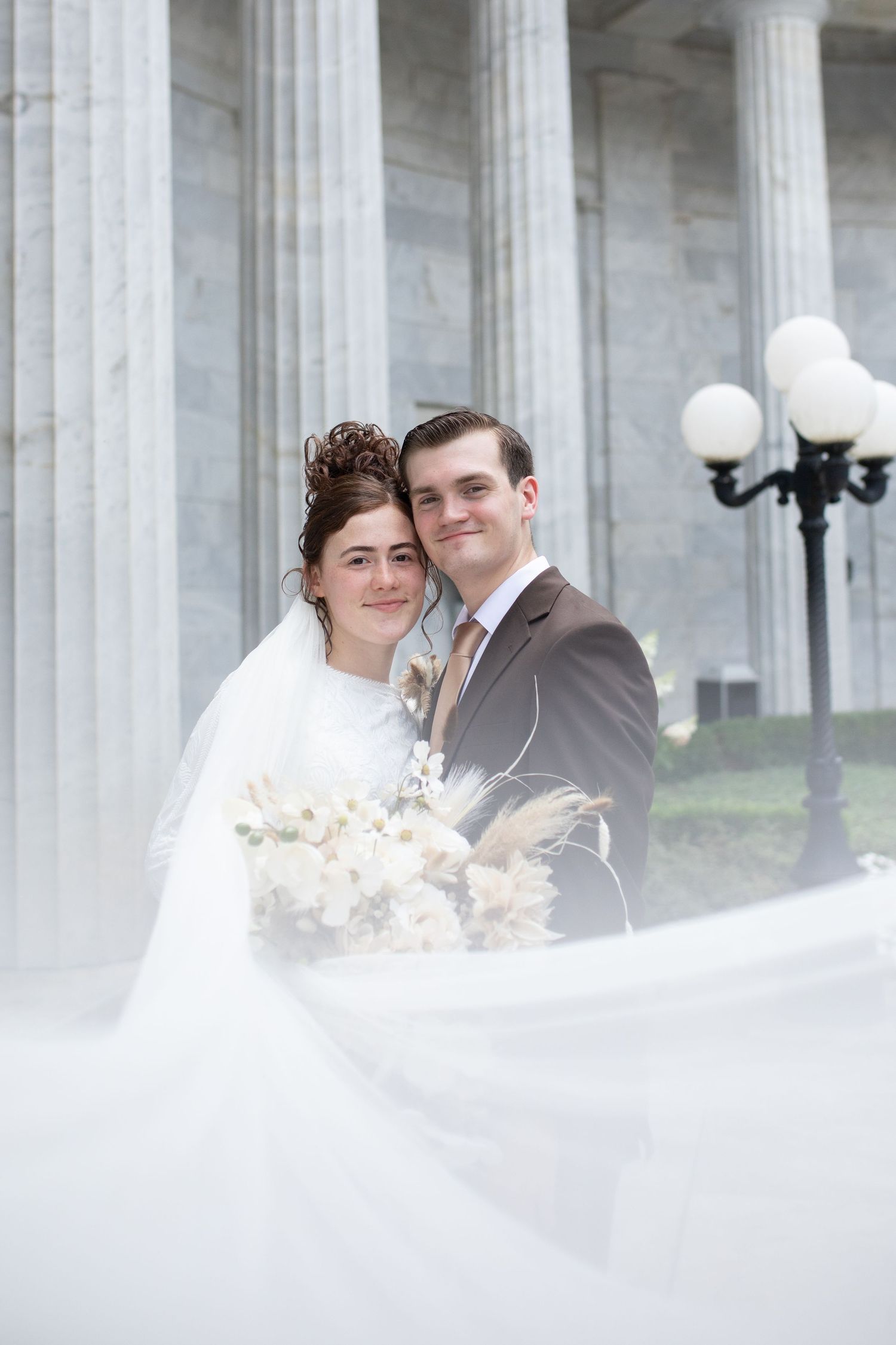Romantic wedding portrait with flowing veil against classical architecture backdrop.