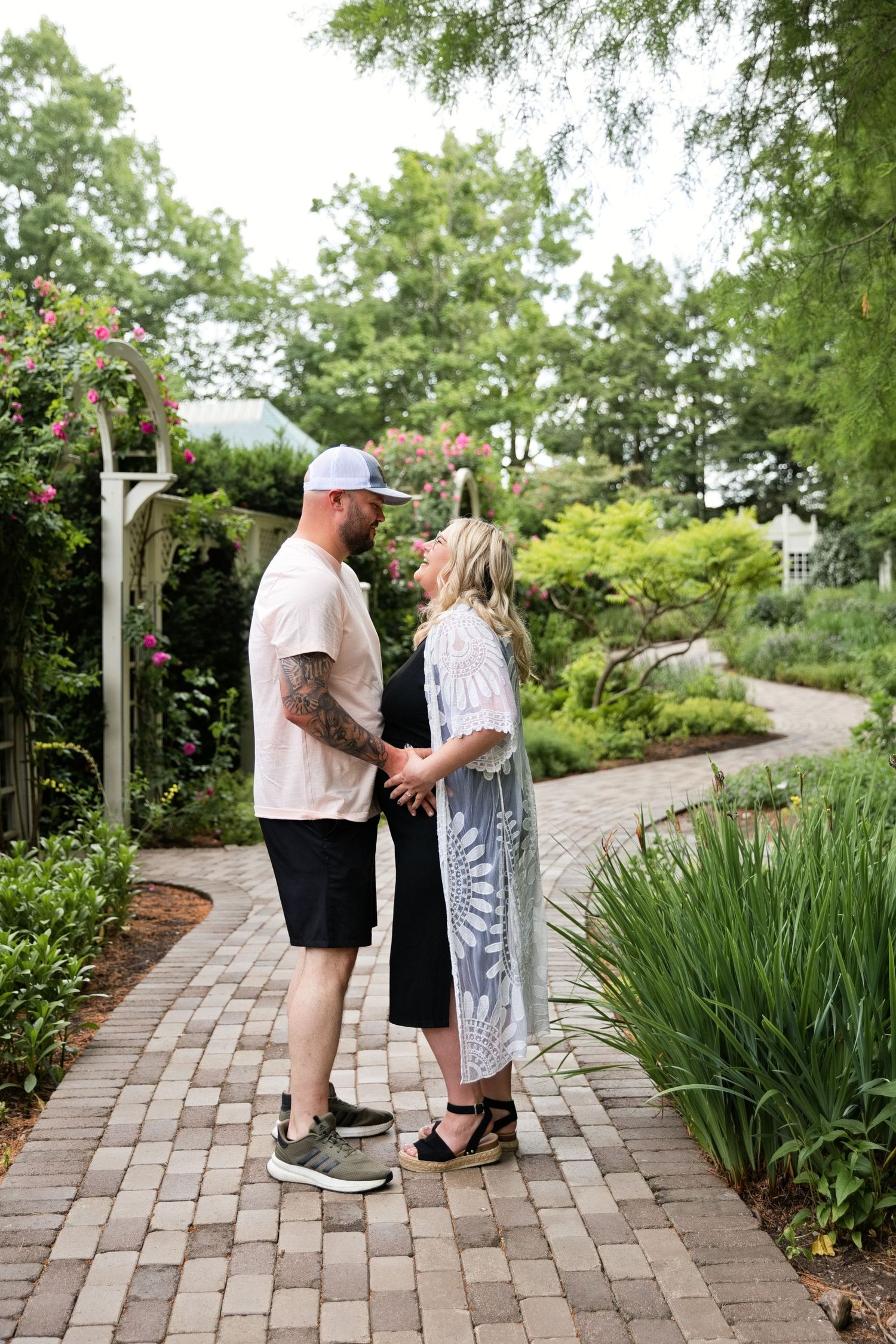 Couple holding hands on a brick garden path surrounded by lush greenery and blooming roses.